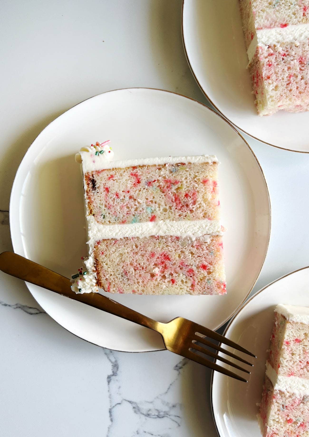 white cake with sprinkles on white plate with gold fork