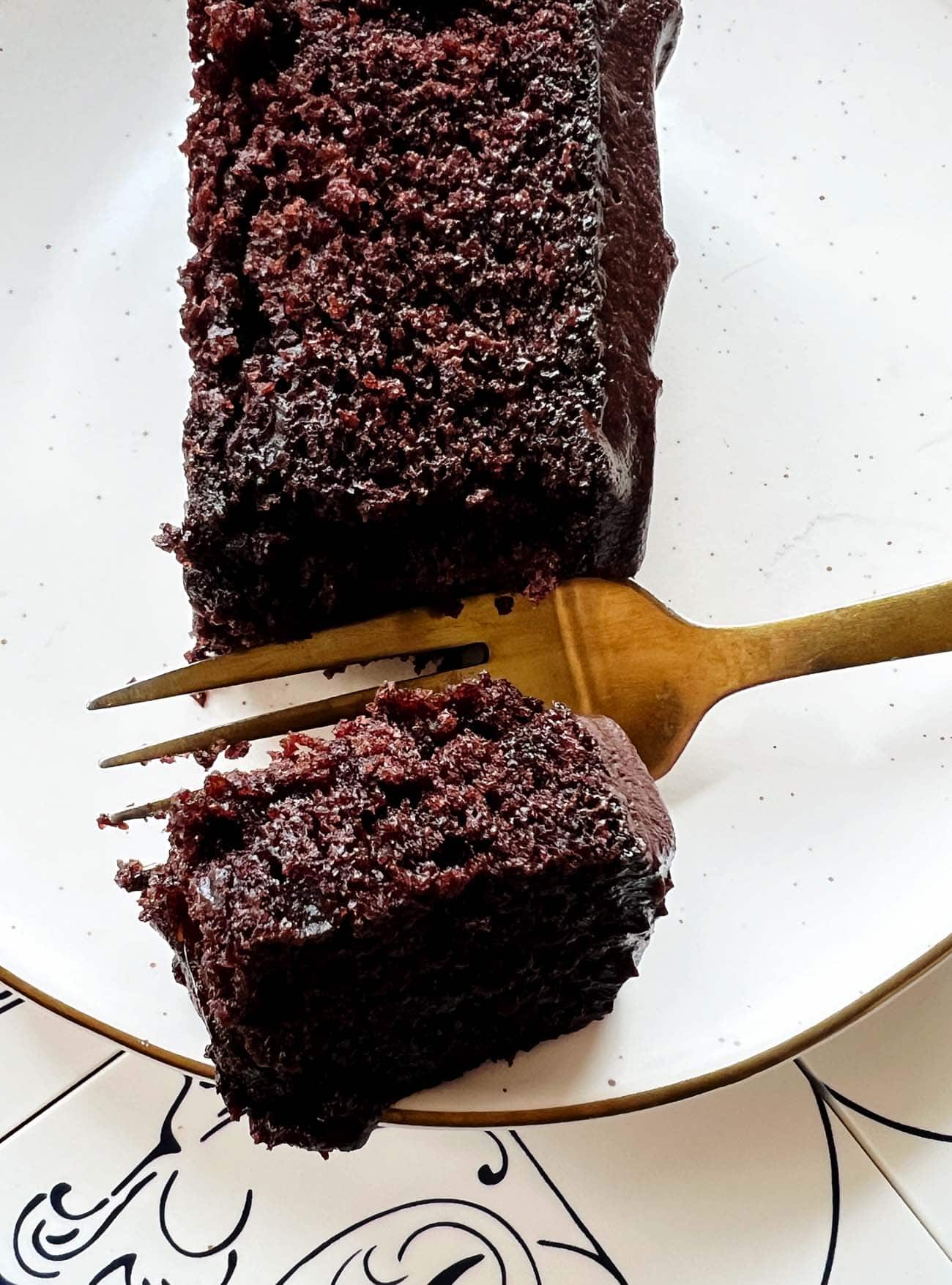 gold fork with piece of chocolate cake on white plate